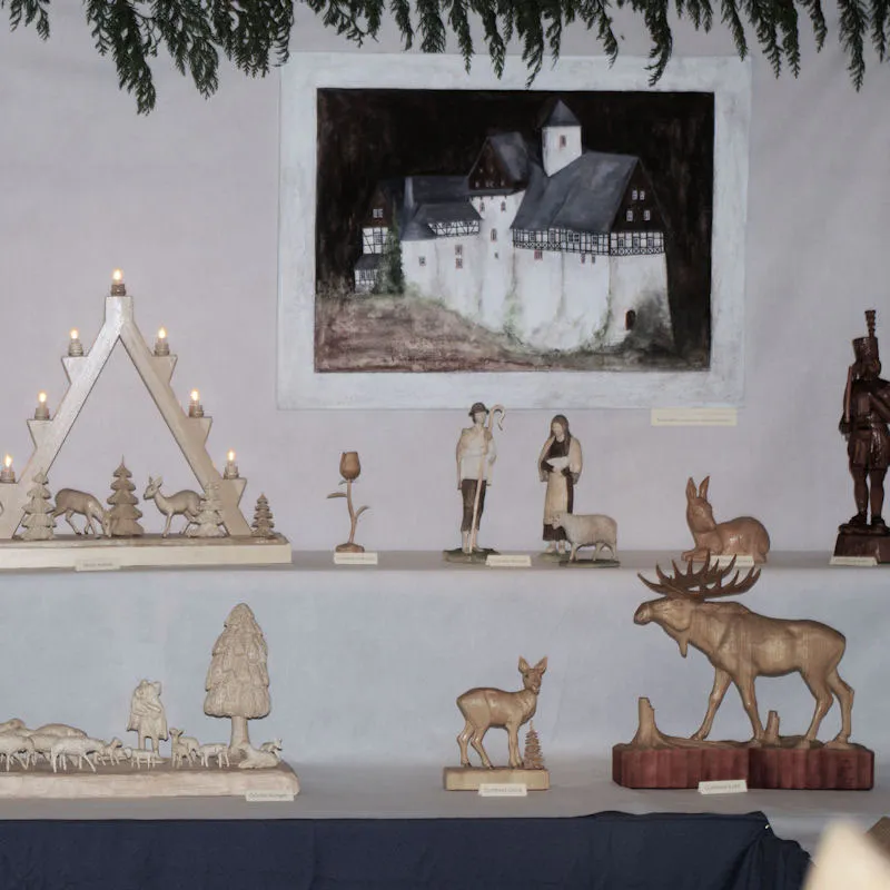 Lichterspitze mit Rehen, davor Schäfer- und Tierfiguren, ein Elch und ein Hase, an der Wand ein Gemälde einer Burg