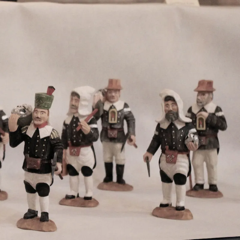 Geschnitzte Bergleute in historischer Tracht mit weißen Kapuzen und Hüten, einer trägt einen Erzbrocken auf der Schulter