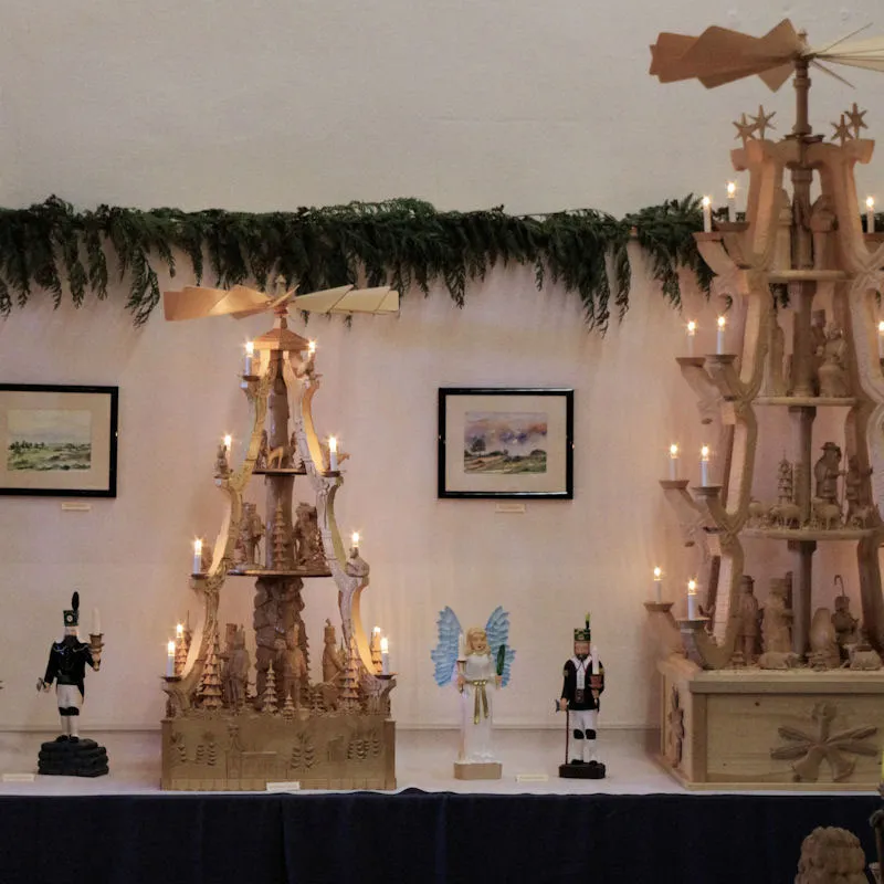 Zwei reich verzierte große Weihnachtspyramiden mit brennenden Kerzen, dazwischen ein Engel mit blauen Flügeln und ein Bergmann