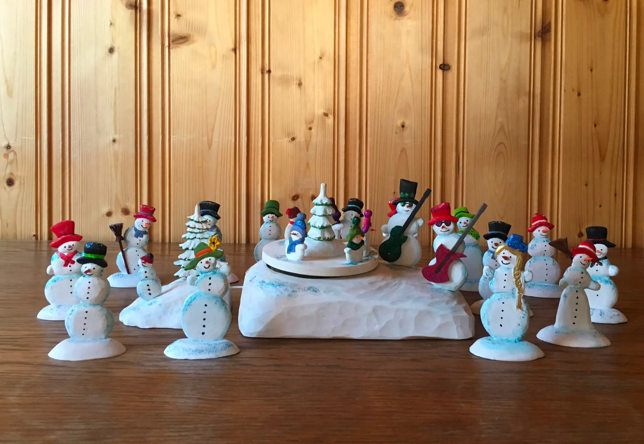 Viele kleine geschnitzte Schneemänner mit bunten Hüten, in der Mitte eine Schneemann-Kapelle auf einer Drehscheibe