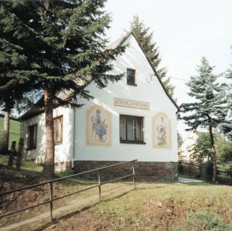 Das Schnitzerhäusel: kleines weißes Haus mit Steinsockel und bemalter Giebelfassade