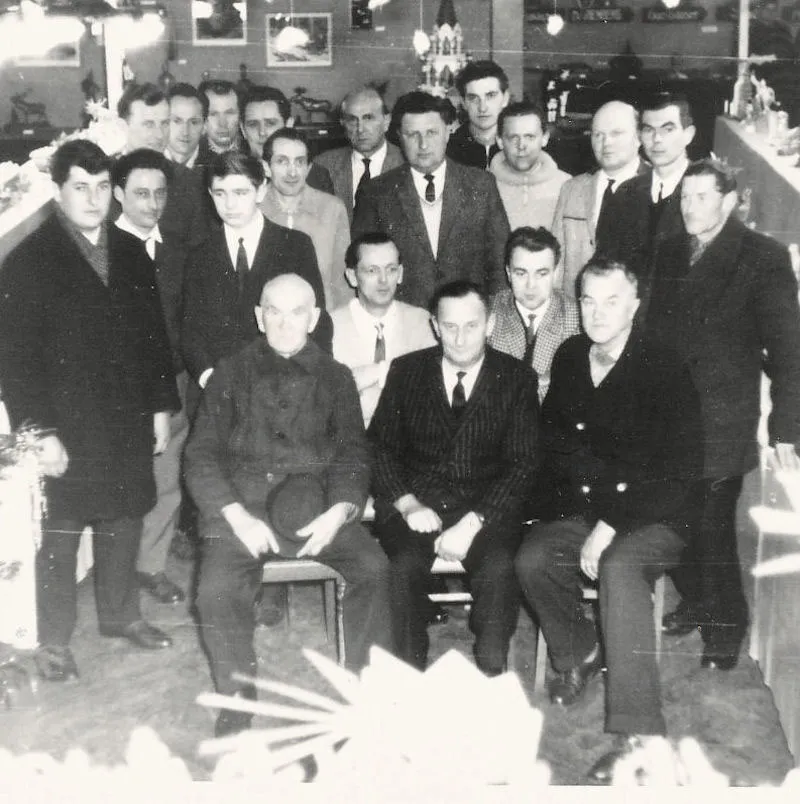 Historisches Schwarz-Weiß-Gruppenfoto: rund zwanzig Männer in Anzügen, aufgenommen zwischen Ausstellungsstücken